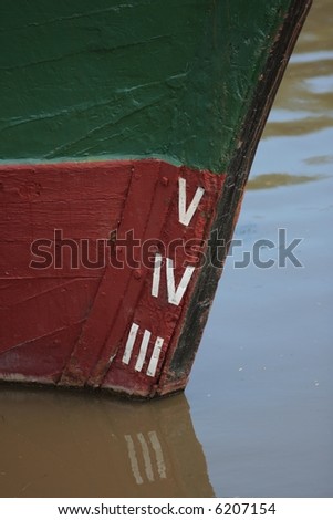 Waterline marks on an old wooden ship, moored in murky river water.
