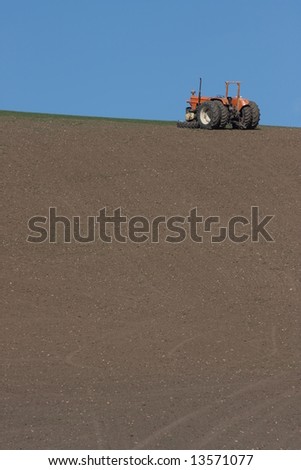 Tractor with missing wheel sitting on the ridge of a hill, waiting for repair.