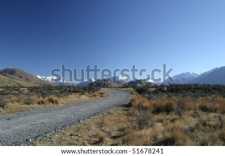 Unsealed road into the distance, Southern Alps of New Zealand in the background, Sunny day