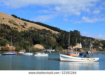 View of Akaroa Harbor, New Zealand, showing recreational boats, a fishing boat and the old restored Lighthouse in the background