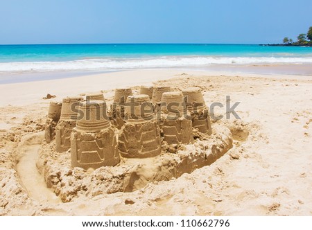 A sand castle at the beach against blue sky and crystal blue water