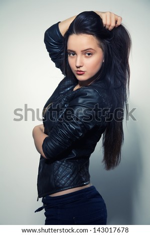 pretty brunette girl in leather jacket smiling at gray background