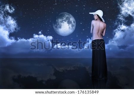 bare woman looking at full moon between clouds over water