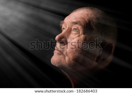 old senior man looking up praying at dark in light rays
