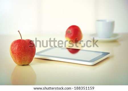 tablet pc with red apples and coffee cup with reflections on table