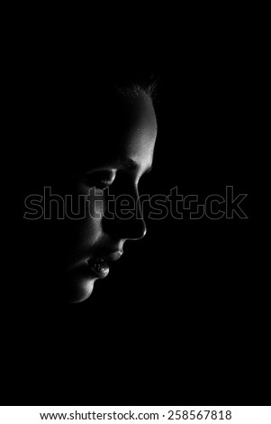 sad young woman profile looking down in dark, monochrome