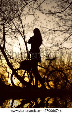 woman with bike silhouette at sunset with reflection in water toned image