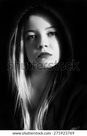 pensive young woman in black hood on black background monochrome