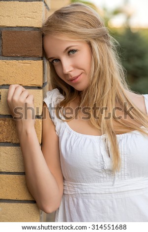 attractive smiling blond young woman near bricks wall