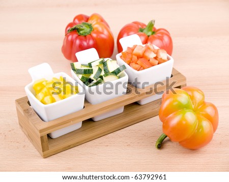 Fresh chopped paprika and zucchini in small porcelain bowls on wooden table