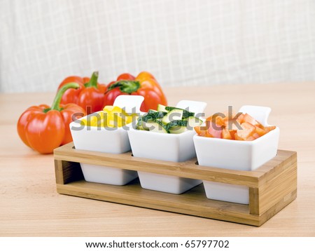 Fresh chopped paprika and zucchini in small porcelain bowls on wooden table