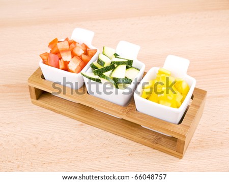 Fresh choped paprika and zucchini in small porcelain bowls on wooden table