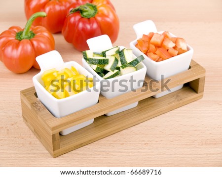 Fresh choped paprika and zucchini in small porcelain bowls on wooden table