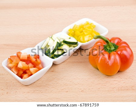 Fresh paprika and zucchini in small porcelain bowls on wooden table