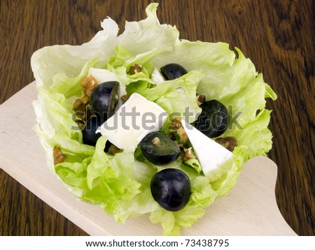 Tasty salad with camembert cheese, dark grapes and walnuts in iceberg lettuce leaf on chopping board