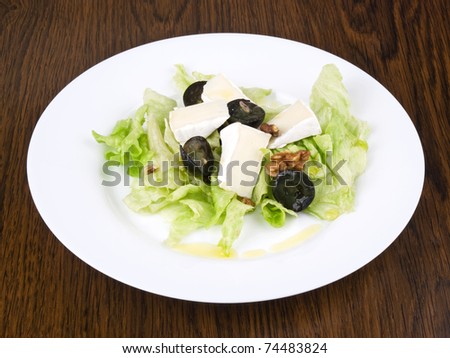 Iceberg lettuce salad with camembert cheese, dark grapes and walnuts on white plate