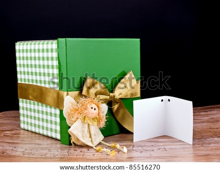 Big green gift box with golden ribbon and little angel on wooden table