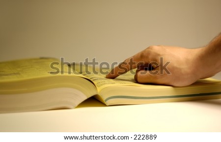 Hand pointing at yellow page ad. Shallow depth of field, focus on hand.
