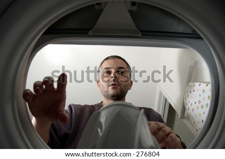 Young man reaching inside washing machine. Unusual angle.
