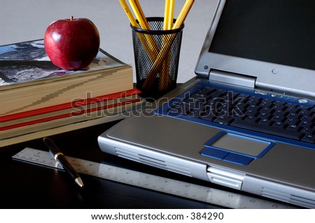 Close-up of laptop, books, ruler, pen, pencils and apple on desk. Natural light hitting from the left.