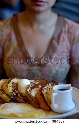 Plate with breakfast. French toast with butter, syrup and eggs. Woman in background.