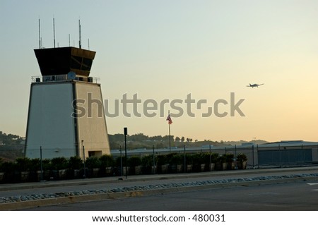 Airport traffic control tower at sunset with small airplane taking off