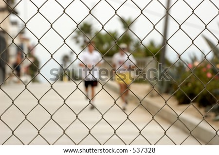 Two men running towards a chainlink fence. Shallow DOF, focus on fence.