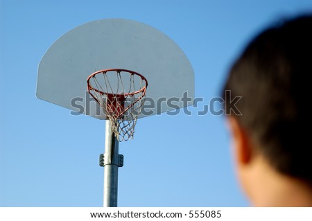 Boy standing in front of basketball hoop looking at it. Shallow DOF, focus on basketball hoop.