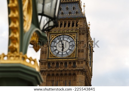 The clock tower in London known as Big Ben. Photo taken from Westminster Bridge with a blur ornamental lamp in front and Big Ben at back.