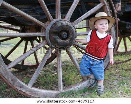 Farmboy:  A baby cowboy hangs out at the wheel of an old farm wagon in a cowboy hat and denim shorts.