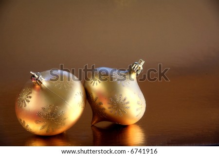 Glittering Gold: Two glittering gold ornaments on a reflective gold background with space for copy.