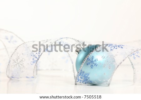 Snowflake Spiral:  An frosty blue ornament lies in a spiral of transparent, glittery snowflake ribbon against a white background. Holiday concept.