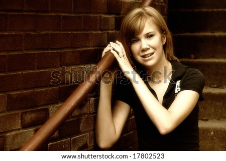 Urban Teen:  A teenage girl sits on a stairway near a brick building in a high contrast sepia image with a slight grain for an edgy, grungy look.