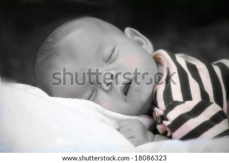 A baby girl naps outdoors on a blanket in classic soft focus with a touch of selective color.