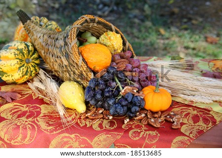 Cornucopia Harvest: A cornucopia overflows with the fruits of a fall harvest on an outdoor table full of autumn color. Seasonal, holiday concept.