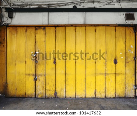 A grungy old yellow color metal folding door on the shopfront of an old workshop.