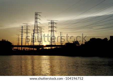 Silhouette of power pylon line from a hydro power plant by a reservoir against a fiery sunset.