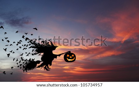 Silhouette of a witch flying on a broomstick carrying a sinister pumpkin lantern with flocks of crow following her during an eerie surreal evening, for Halloween concept.