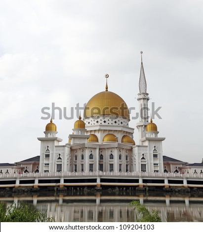 A vintage medieval golden dome islamic mosque on a river bank with reflection, on a blue cloudy day in the Royal Town of Klang, Malaysia.