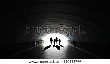 Silhouette of a family comprising the father, mother and two children walking into the light at the end of an underground tunnel.