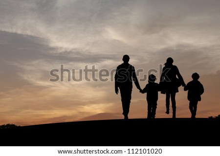 Silhouette of a family comprising a father, mother and two children walking into the sunset.