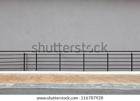 A blank grey concrete wall with hand railing on a roadside walkway.
