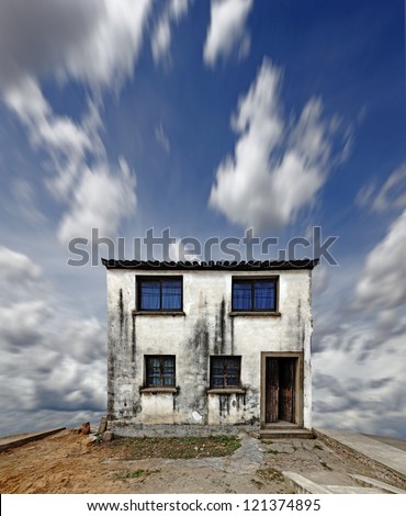 An individual weathered concrete house against a blue cloudy sky for the concept of foundation of a home.