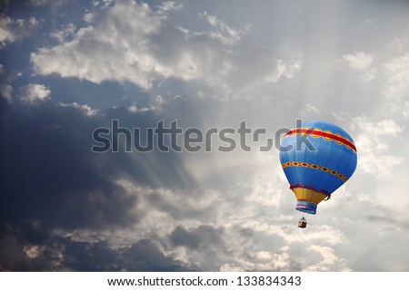 A colorful vintage hot air balloon floating in a surreal morning sky with sunshine bursting through the clouds.