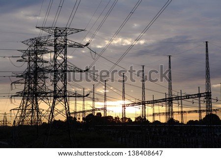 Silhouette of electricity power pylon line at a rural power distribution grid against a fiery sunset.