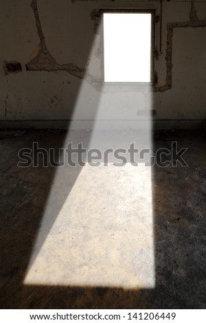 A beam of sunlight shinning from a rectangular window brightening a dark dilapidated room.