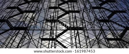 Chaotic pattern of industrial climbing scaffold frame silhouette against a dreamy blue cloudy sky.