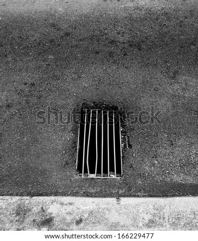 A grungy metal grate of a manhole to an underground drainage system on a asphalt road.