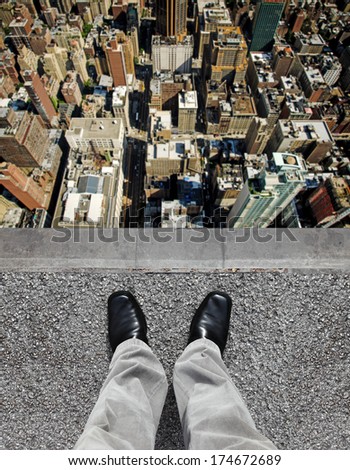 A pair of feet on the edge of a tall building ledge looking down into a city of highrise.