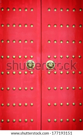 Red exotic vintage imperial chinese palace gate with ornamental brass stud and traditional lion head knocker.
